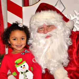photo - little girl, smiling, in red shirt, with snowman image on front, with Santa Claus, in his red suit, everyone is smiling