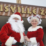 banner - mr & mrs claus, main plaza, zoo entrance, dressed in christmas red outfits, santa has long white beard, mrs. claus wearing her xmas bonnet, smiling, holding hands