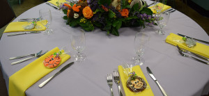 banner - social events, table setting for 6, with flowers on table, animal cookies laying on yellow napkins, silverware settings, with short stem glasses