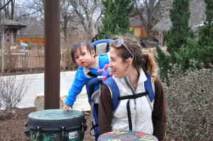 photo - mother, with child in a backpack carrier, trying to play drums at the outpost