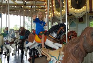 photo- day camper riding horse, smiling, waving, while on the carousel