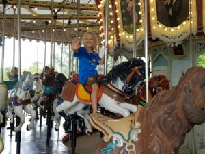 photo- day camper riding horse, smiling, waving, while on the carousel