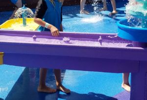 photo - young child playing in water element waterfall, while playing in the splash park on a sunny summer day