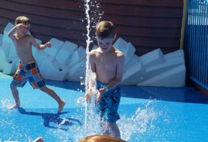 photo - young man playing with in ground water spout, in splash park, on a sunny summer day
