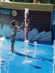 photo - young man playing with inground water spouts, while in the splash park, on a sunny summer day