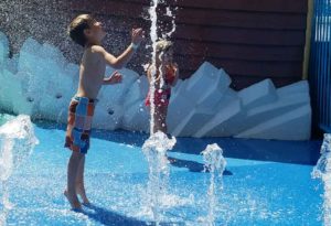 photo - young man playing with inground water spouts, while in the splash park, on a sunny summer day
