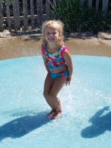photo - little girl, in pretty bathing suit, smiling, playing in the zoo splash park on a sunny summer day