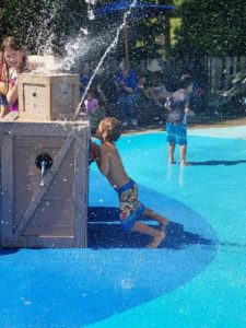 photo - young man, playing with spouting water element, in splash park on a sunny summer day