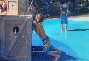 photo - young man, playing with spouting water element, in splash park on a sunny summer day