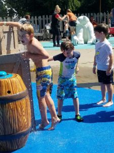 photo - young boys playing with water spout element inside zoo splash park on a sunny summer day