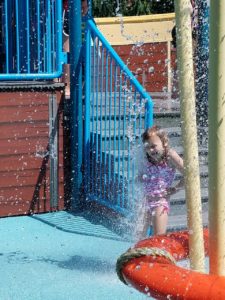 photo - young girl playing among the inground water spouts at zoo splash park, on a sunny summer day