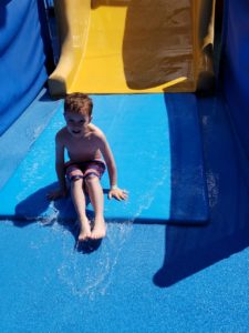photo - young boy, who slid down yellow splash park slide, on a sunny summer day
