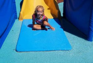 photo - young girl, who slid down, yellow splash park slide, on a sunny summer day