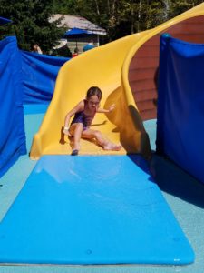 photo - young girl, going down yellow splash park slide, on a sunny summer day