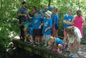 photo - group of day campers, at wetlands bridge, with counselor giving a presentation on what they can find in the water