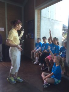 photo - docent giving a presentation about raptor she is presenting to group of Safari day campers, as kids raise their hands to answer/ask questions