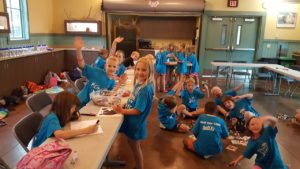 banner - group of zoo day campers, doing arts and crafts, with coloring, stampers of animals and designs, in the kitchen of glacier run (?) building at zoo, sitting at tables, on floor, waving, and having a good time