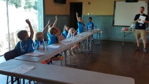 photo - group of Safari day campers, in classroom, with counselor Josh, raising their hands to answer questions asked by josh