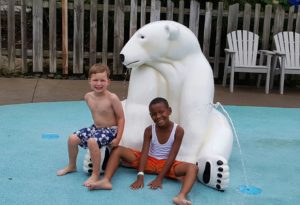 photo - two boys, in swim trunks, sitting in front of the polar bear white statue, on the pad of the splash park