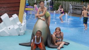 Safari day campers enjoying themselves in splash park among the ground water spouts, on the slides and statues in the splash park, they are all smiling too