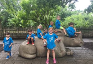 photo - Safari day campers, boys and girls, sitting on the rhino statue in the zoo, all wearing blue t shirts, penguin cove