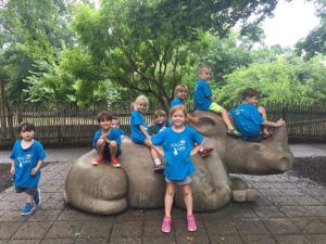 photo - Safari day campers, boys and girls, sitting on the rhino statue in the zoo, all wearing blue t shirts, penguin cove