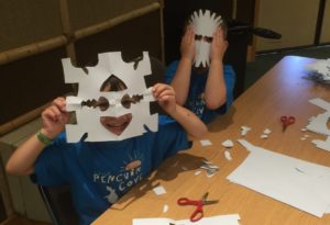 photo - Safari day campers, cutting out shapes from folded paper, to make different designs, when you unfold said papers, it will make a mask for camper to wear.