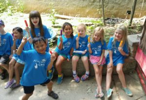 photo - zoo day campers, boys and girls, in blue t-shirts, having popsicles on hot summer day, sitting on stone wall