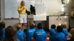 photo - zoo docent, displaying whale vulture, to class of zoo day campers, blue t-shirts, making a presentation about the bird