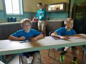 photo - two boys, zoo day campers, paying attention to directions maybe, what to do with paper in front of them. zoo counselor in background