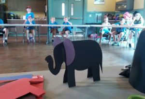 photo - classroom of zoo day campers, sitting at tables, with closeup of zoodunnit elephants that were made using paper and scissors
