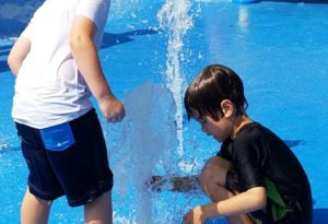 photo - boys playing with popup water spouts, at zoo splash park, background are other water spouts with kids playing