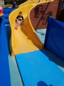 photo - small boy, in t shirt and swim trunks, sliding down yellow water slide, in zoo splash park water park