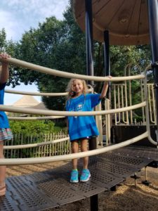 photo - young girl, in zoo camper blue t-shirt, standing on crossing bridge on playground equipment in zoo playground