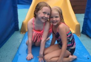 photo - young girls, in swimsuits, sitting at end of water slide, smiling, inside splash park water park at zoo
