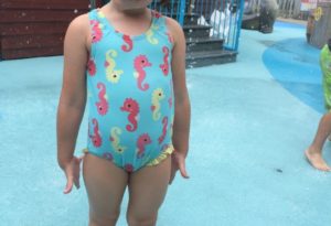 photo - little girl, in seahorse blue swimsuit, standing in splash park area