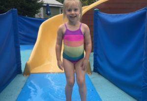 photo - little girl, in swimsuit, standing in splash park water slide,