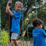 photo - two small children having fun on playground equipment, in blue day camp t-shirts