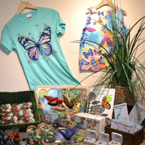 image - gift shop items to purchase of butterfly themed t shirts, pillows, books, jewelery, prints, earrings, snow globes, all the butterflies on these items are multi colored wings, large and small, very spring themed with the colors