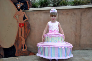 photo - little girl dressed as a 3 tier pink cake from movie Beauty and the Beast, with Mowgli card board stand behind the little girl