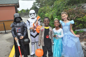 photo - 4 children in costumes Darth Vader, Storm trooper, princess in blue ball gown, another princess in aqua colored princess dress with jeweled crown, another super hero dressed in black, with silver jacket, holding plastic pumpkin heads, black kettle for darth vader