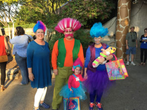 photo - family of 4 individuals dressed in costumes as cartoon character trolls, there are blue, pink , purple, trolls hair, plus small child in blue tutu, red shirt, with pink troll hair