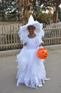 photo -young girl wearing white witch's costume, with white witch hat, holding plastic orange pumpkin for collecting candy