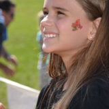 photo - young girl with flower tattoo on cheek, smiling, with a orange/black monarch butterfly sitting on her giner
