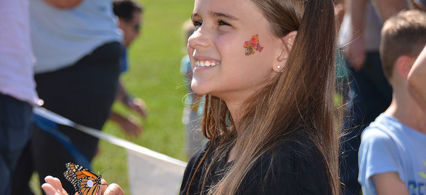 photo - young girl with flower tattoo on cheek, smiling, with a orange/black monarch butterfly sitting on her giner