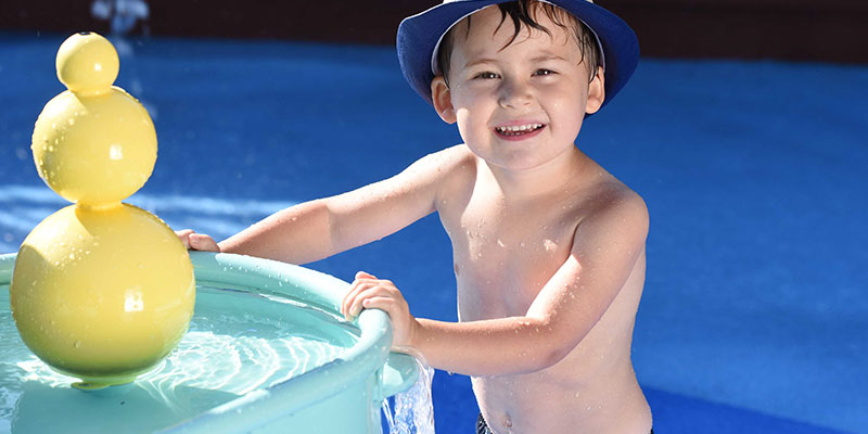 photo - little boy, wearing blue hat, playing with splash park toys at the splash park