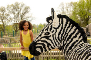photo - lego black and white zebra, head shot, with young girl standing and laughing next to it