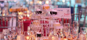 banner - of zoofari table setting with variety of champagne glasses, with display stand of variety of chocolate, vanilla iced cupcakes, background is of other tables at the event