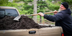 photo - an individual, in blue hoodie, black cap, using shovel to move zoo poop doo in bed of pickup truck for ZooPoopyDoo Sale 2023
