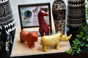 photo - gift shop items - african crafted wooden animals, each with intricate designs on them - orange lion, yellow rhino, brown giraffe, with variety of african crafted vases with intricate animal, print designs on them, information framed print about the crafts
